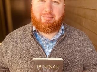 Persona sosteniendo el libro «Runes of Wrath and Ruin» (Runas de ira y ruina), de E. C. Lee, frente a un fondo de pared de madera.