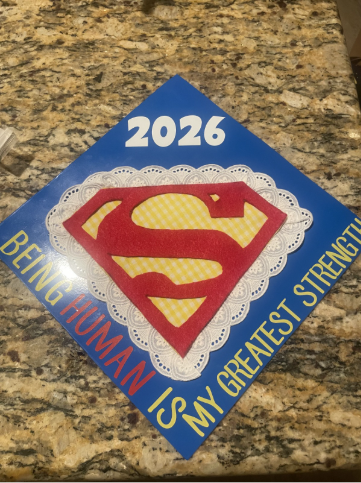 Un birrete de graduación decorado con el símbolo de Superman y la frase «Ser humano es mi mayor fortaleza».