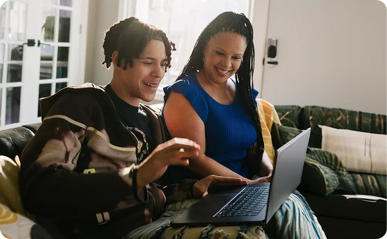 Un estudiante con su madre, trabajando con su ordenador portátil